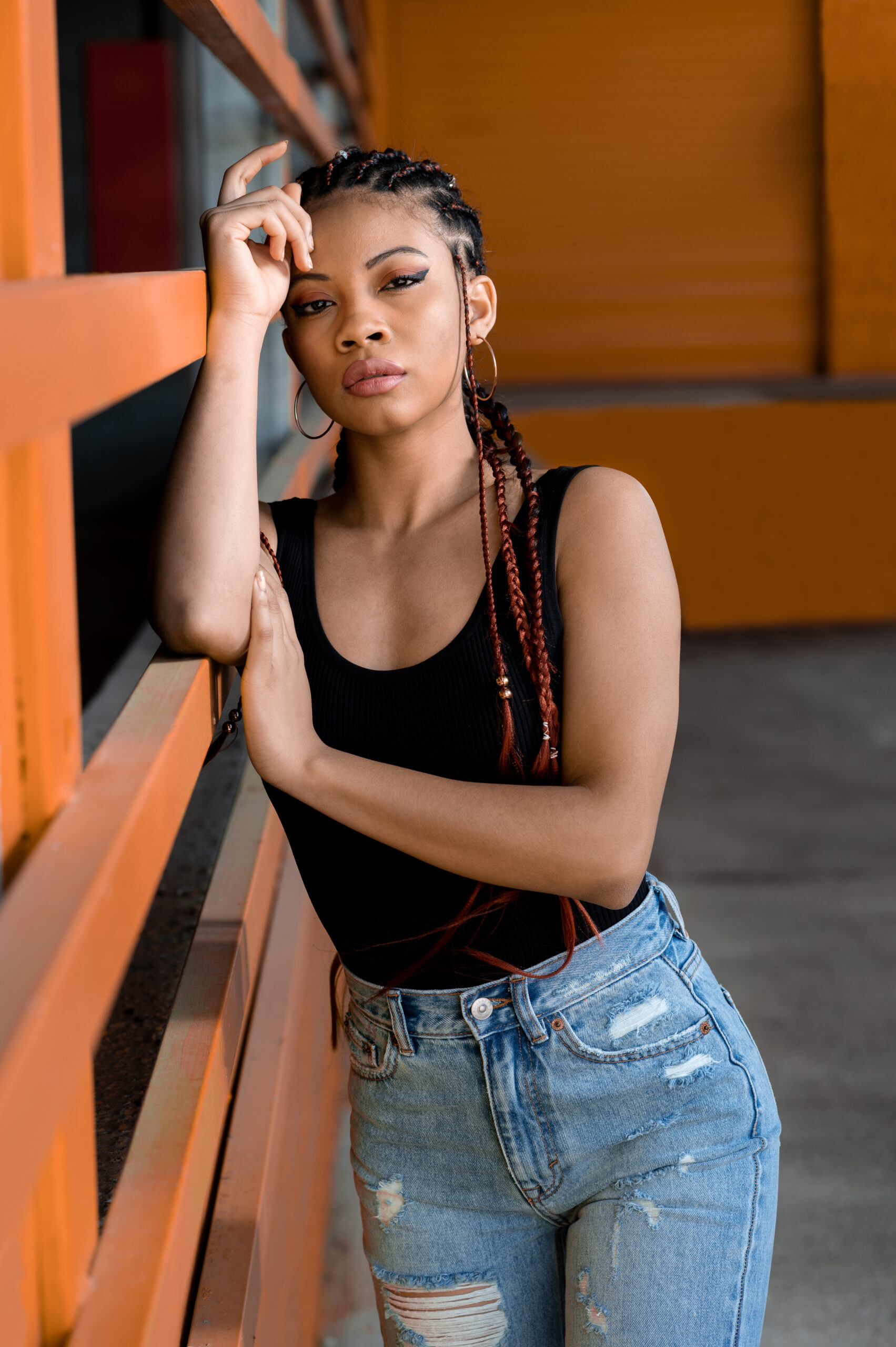 A vertical shot of a cool young Afro-American lady with deads leaning on an orange construction